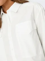 Camisa blanca de corte cropped, con cuello clásico, mangas largas con puños abotonados y dos bolsillos de parche en el pecho.