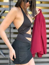 Body negro con escote halter, espalda descubierta, abertura en la cintura con detalle de hebilla dorada y falda corta negra con brillos y nudo lateral.