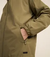 Campera rompevientos color verde oliva, con capucha ajustable con cordón, cierre frontal con cremallera, bolsillos laterales con cremallera y puños elásticos.