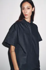 Camisa de denim azul oscuro, de corte recto, con cuello clásico, manga corta y cierre frontal con botones.