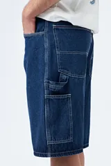 Bermuda carpenter de denim negro, corte relajado y largo a la rodilla, con costuras visibles y múltiples bolsillos funcionales.