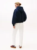 Buzo con capucha Tommy Hilfiger azul marino de corte amplio, confeccionado en tejido de felpa flexible de mezcla de algodón. Presenta logo texturizado en fuente script en el pecho, puños y bajo de punto canalé, cordón en la capucha y logo bordado en la manga.