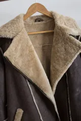 Campera gamulán marrón con interior de piel sintética color beige, cierre cruzado con cremallera y cuello con solapas amplias.