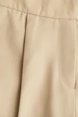 Short pollera corto color beige, de estilo sastre, con pinzas frontales, pretina prolongada con corchetes y bolsillos al bies.