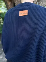 Sweater de tejido de punto color beige, con cuello redondo y manga raglán. Presenta un bordado en hilo rojo con un monograma en el pecho.