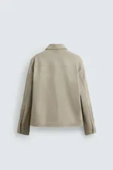 Sobrecamisa color arena de corte relaxed fit, confeccionada en tejido con mezcla de algodón. Tiene cuello solapa, manga larga con puños abotonados, bolsillos de plastrón con solapa en el pecho y bolsillos laterales en la costura de la cadera. El cierre es frontal con cremallera.