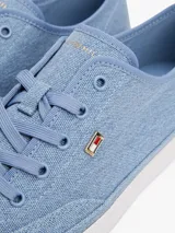 Zapatillas de lona de corte bajo, color celeste claro con efecto lavado, suela de goma blanca y cordones a tono. Presentan un pequeño logo esmaltado de Tommy Hilfiger en el lateral exterior.