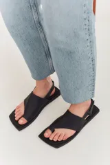 Sandalias de cuero color crema con tira ancha sobre los dedos, suela plana cuadrada color negro y tira trasera ajustable.