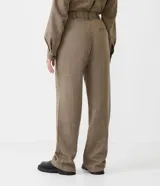 Pantalón de vestir de corte ancho, color marrón con textura tweed. Tiene cintura alta con trabillas, pliegues frontales, bolsillos laterales y un bolsillo trasero.