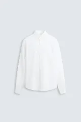 Camisa blanca de corte regular fit confeccionada en popelín de algodón. Tiene cuello abotonado, manga larga con puños abotonados y cierre frontal con botones.