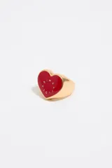 Anillo dorado con forma de corazón rojo y letras doradas.