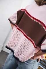 Remera de tejido calado color crudo con rayas horizontales rojas y terminaciones marrones, con cierre frontal y logo bordado.