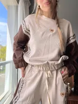 Conjunto deportivo de buzo y jogging color beige con mangas marrones y detalles de estampado animal print. El buzo tiene cuello redondo, mangas largas con puños elásticos y cintura ajustable con cordón. El jogging tiene cintura elástica con cordón ajustable, bolsillos laterales y detalle de estampado animal print en los laterales.