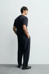 Pantalón de denim azul oscuro, corte wide fit, largo cropped, con pliegues frontales, bolsillos laterales y traseros asimétricos. Cierre frontal con cremallera y gancho metálico oculto.