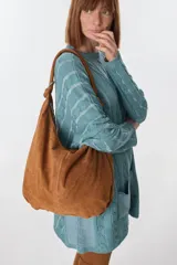 Bolso tipo hobo de cuero color visón con cierre superior y correa de hombro.