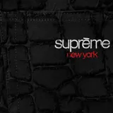 Short de jean negro con textura de piel de cocodrilo y terminaciones desflecadas. Modelo de la marca Supreme con dos bolsillos frontales y etiqueta roja con el logo en la cintura.