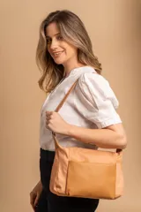 Bandolera de diseño moderno, color beige rosado, con correa regulable y bolsillo frontal con cierre.