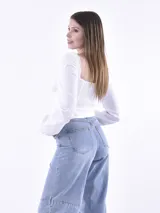 Blusa blanca de estilo milkmaid con escote cuadrado ribeteado en puntilla, detalle de busto fruncido y mangas largas abullonadas.