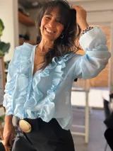 Camisa celeste de organza con volados frontales y en las mangas largas abullonadas.