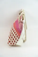 Bolso tipo tote con diseño de bloques de color rosa, rojo y blanco con estampado de lunares y textura tejida. Asas de soga gruesa.