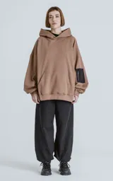 Hoodie marrón de algodón rústico con silueta oversize, capucha forrada, bolsillo tipo canguro y bolsillo en la manga con cierre.