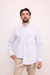 Camisa celeste con rayas verticales blancas, de corte clásico, con cuello abotonado, manga larga y bolsillo en el pecho.