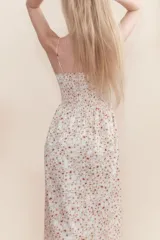 Vestido midi blanco con estampado floral en tonos naranja y marrón. Tiene breteles finos, escote recto y cuerpo fruncido con elástico en el busto.