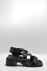 Sandalias negras con tiras cruzadas, hebilla dorada y taco ancho.