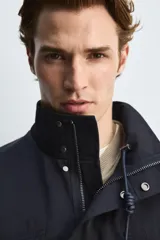 Parka azul marino de tejido técnico, corte relaxed fit, cuello alto ajustable con cordón, manga larga con puños abotonados, cierre frontal con cremallera oculta y solapa con botones a presión, cintura ajustable con cordón interior y bolsillos frontales multifunción de plastrón.