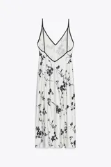 Vestido largo blanco con estampado de flores negras, escote pico y tirantes finos con ribete negro.