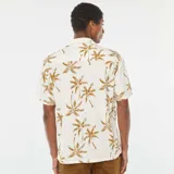 Camisa de manga corta blanca con estampado de palmeras marrones, cuello clásico y cierre con botones.