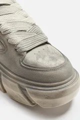 Zapatillas bajas color gris claro con cordones y suela gruesa con diseño irregular.