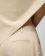 Pantalón tobillero color beige, de corte recto, con trabillas, bolsillos laterales y bolsillos de vivo en la espalda.
