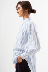 Blusa blanca con finas rayas verticales azules, cuello alto con volado y cierre frontal de botones. Mangas largas abullonadas con puños ajustados.