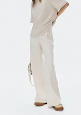 Pantalón de mezclilla color beige claro, de tiro alto y corte ancho (wide leg) que cae recto y amplio hasta el suelo. Presenta cierre frontal y bolsillos laterales.
