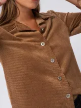 Camisa marrón de pana con cuello camisero, corte recto, mangas largas abullonadas con puños abotonados y cierre frontal con botones.