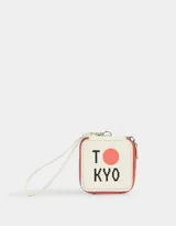 Monedero cuadrado de cuerina color crema con borde rojo, cierre superior y correa de mano. Estampado frontal con la palabra "TOKYO" en negro y un círculo rojo que reemplaza la letra "O".