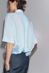 Camisa marrón de corte recto, con cuello solapa, manga corta y cierre frontal con botones.