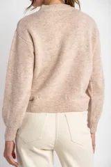 Sweater color beige con cuello redondo y mangas largas. Presenta bordados de flores en tonos marrones en la parte superior delantera.