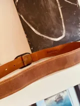 Cinturón marrón de cuero con hebilla ovalada dorada.