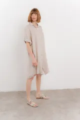Vestido camisero corto color verde oliva, confeccionado en lino 100%. Tiene botones en la parte delantera, cuello camisero, mangas cortas con botón para arremangar y bolsillos laterales.