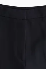 Pantalón negro de vestir, de tiro alto con piernas holgadas rectas con pliegue. Cierre con corchete oculto.