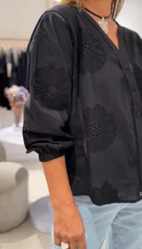 Camisa negra de manga larga con puños elásticos, cierre frontal con botones y detalles de bordados perforados a tono en la parte delantera y trasera.