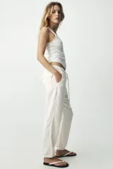 Pantalón jogger color gris claro, de tiro alto con cintura elástica ajustable con cordones, bolsillos delanteros y traseros con solapa, y puños elásticos en los tobillos.