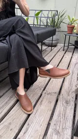 Mocasines marrones de cuero con elásticos laterales y tirador trasero.