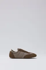 Zapatilla tipo slip-on de caña baja, con capellada combinada en tonos marrón oscuro (capellada y puntera de gamuza) y beige acolchado (zona central). Posee un pequeño detalle en blanco en el talón.