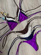 Conjunto de bikini rojo con corpiño triangular con tirantes finos y detalle de aro metálico con forma de corazón en el centro. La bombacha es tipo colaless con tiras finas ajustables en los laterales con detalle de aros metálicos.