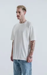 Remera oversize de algodón premium color blanco tiza, con cuello redondo rib al tono y hombros caídos.