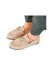 Mocasín color avena de cuero gamuzado con lazo frontal y detalle de pasacintas laterales. Suela flexible antideslizante.