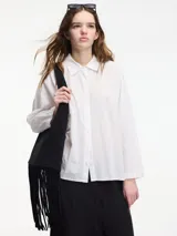 Camisa blanca de algodón con cuello camisero y botones frontales.